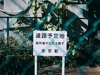 フェンス越しの東京都の道路予定地看板の無…